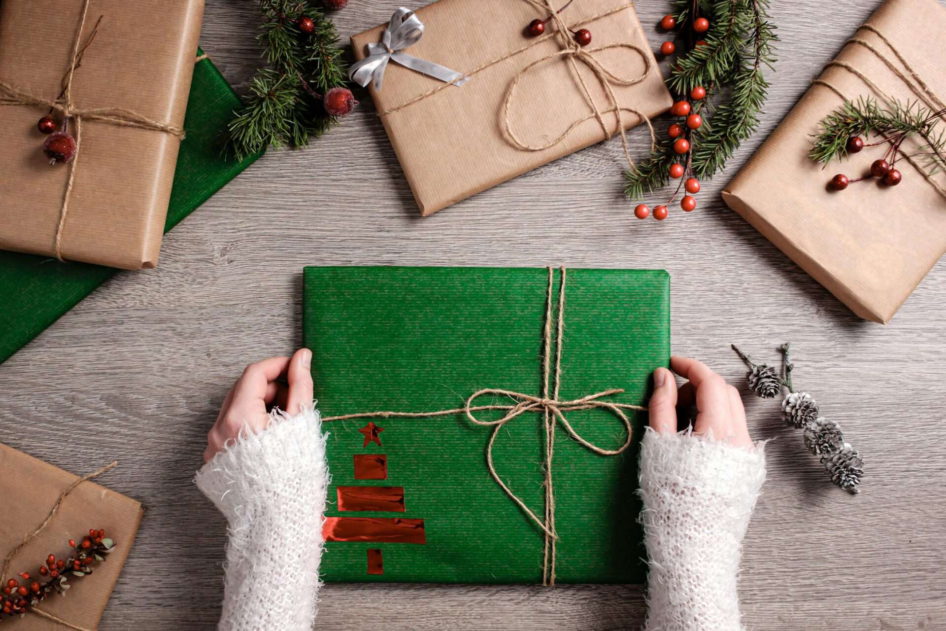 Top view of Christmas gifts wrapped in green and brown paper with festive decor.