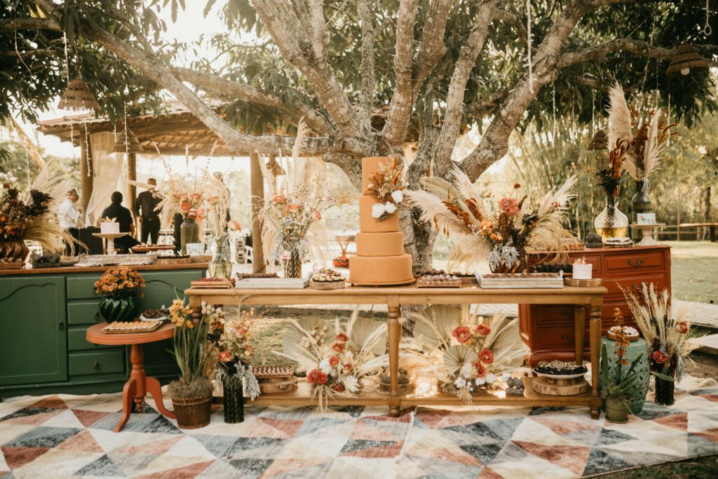 Boho-chic wedding reception setup outdoor with floral decor and layered cake.